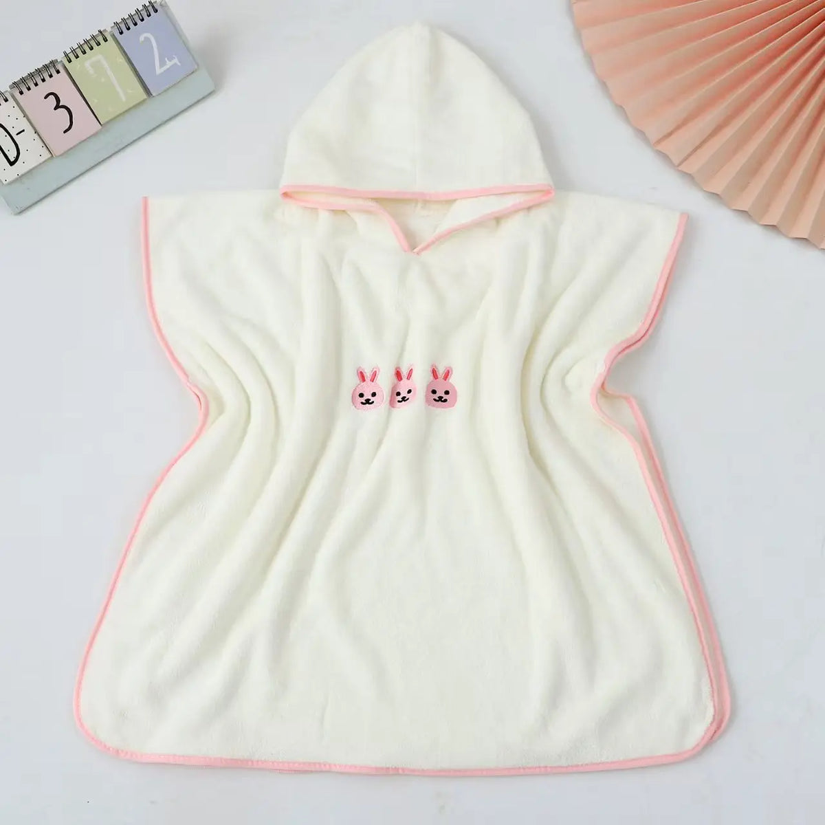 Posé à plat, coloris écru bordé de rose, capuche et petits lapins brodés