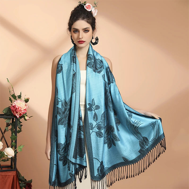 Femme déployant le poncho écharpe bleu ciel à fleurs sombres, un pan tenu à la main