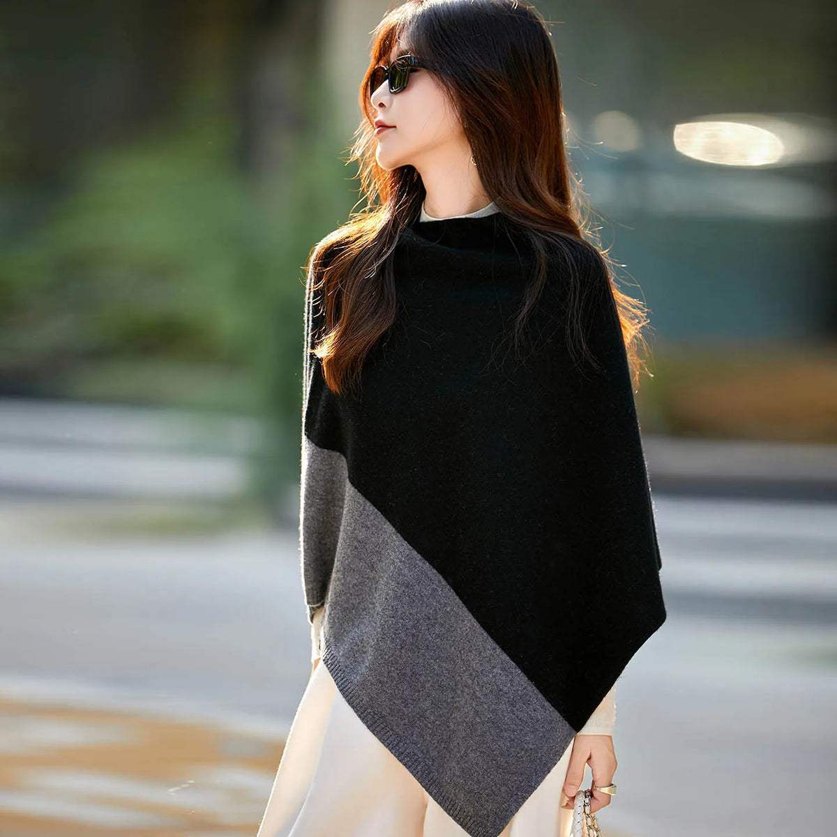 Femme en poncho noir à panneau gris contrasté, col montant et pointe asymétrique, en ville