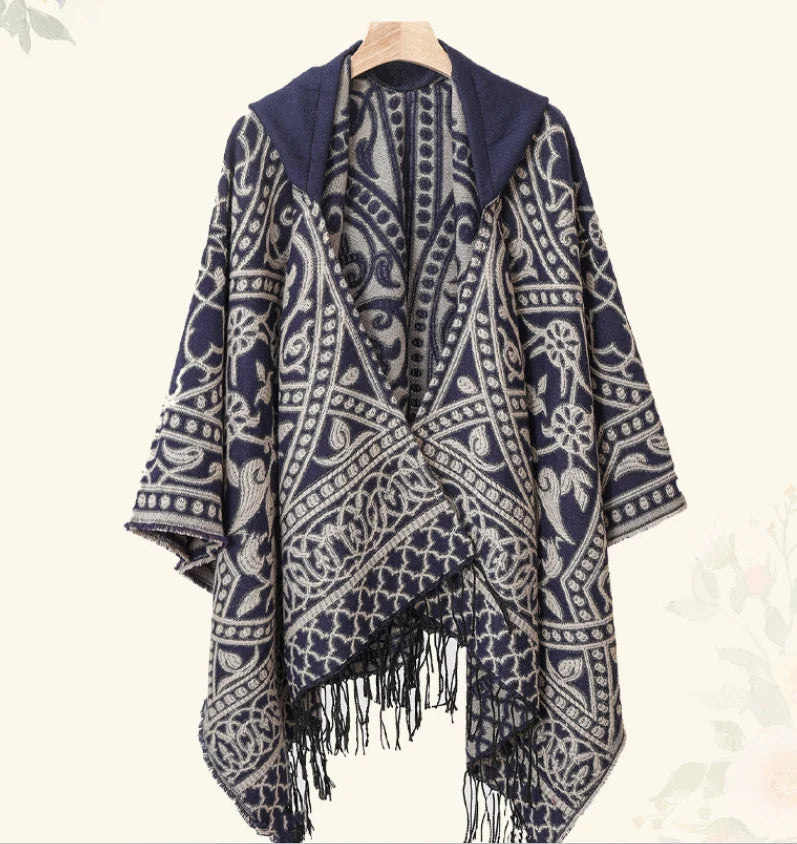 Poncho jacquard bleu marine et écru sur cintre en bois, capuche rabattue et franges en bas