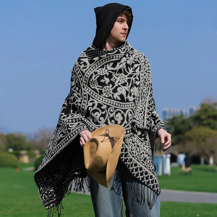 Homme portant le poncho jacquard noir et écru, capuche relevée, franges sur le côté