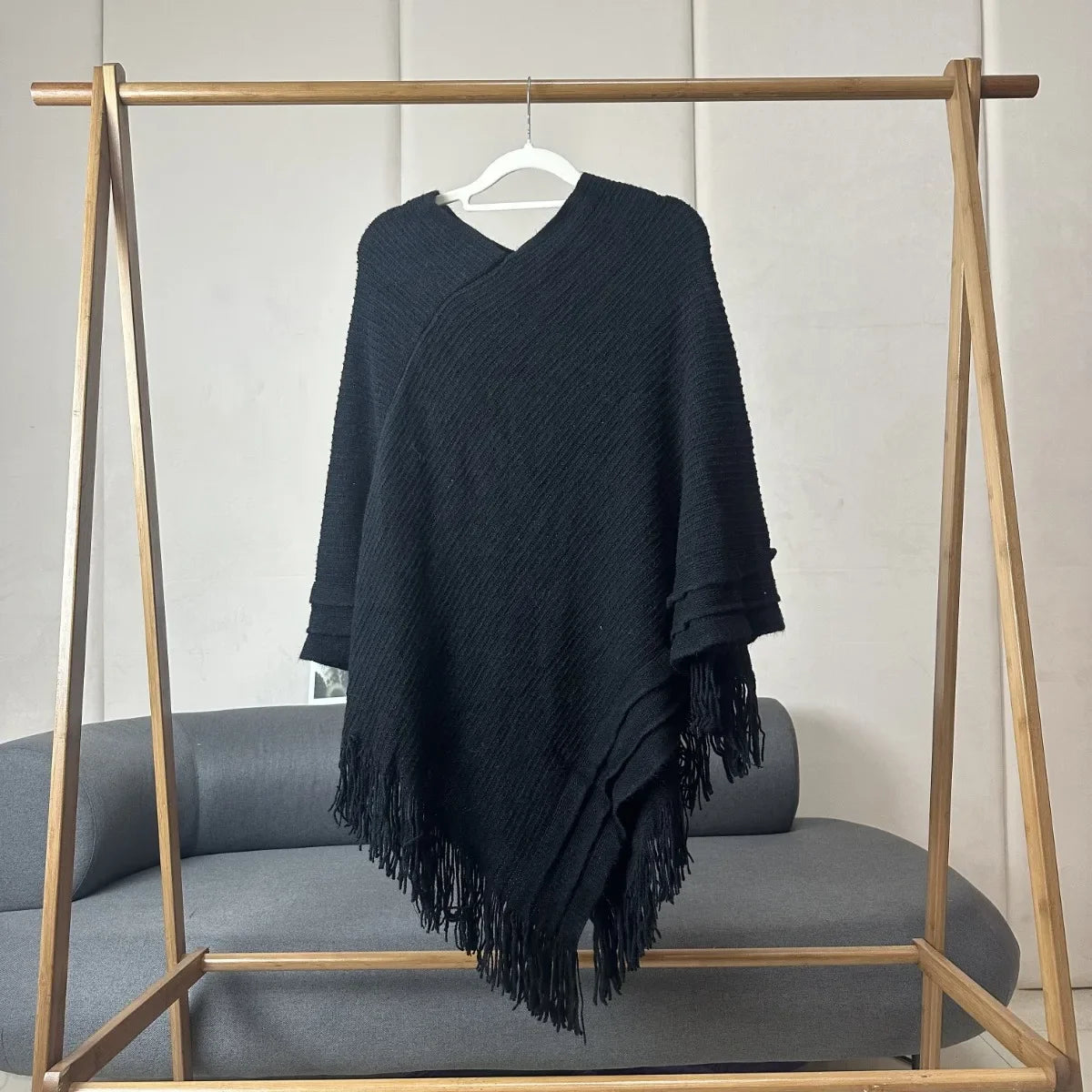 Poncho pull noir en maille côtelée à franges, pointe descendante, sur cintre en bois